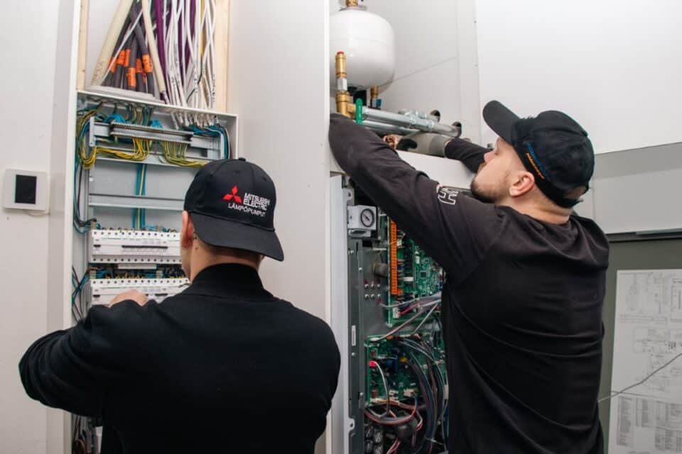 Kaksi asentajaa tekemässä töitä ja asentamassa maalämpöpumppua